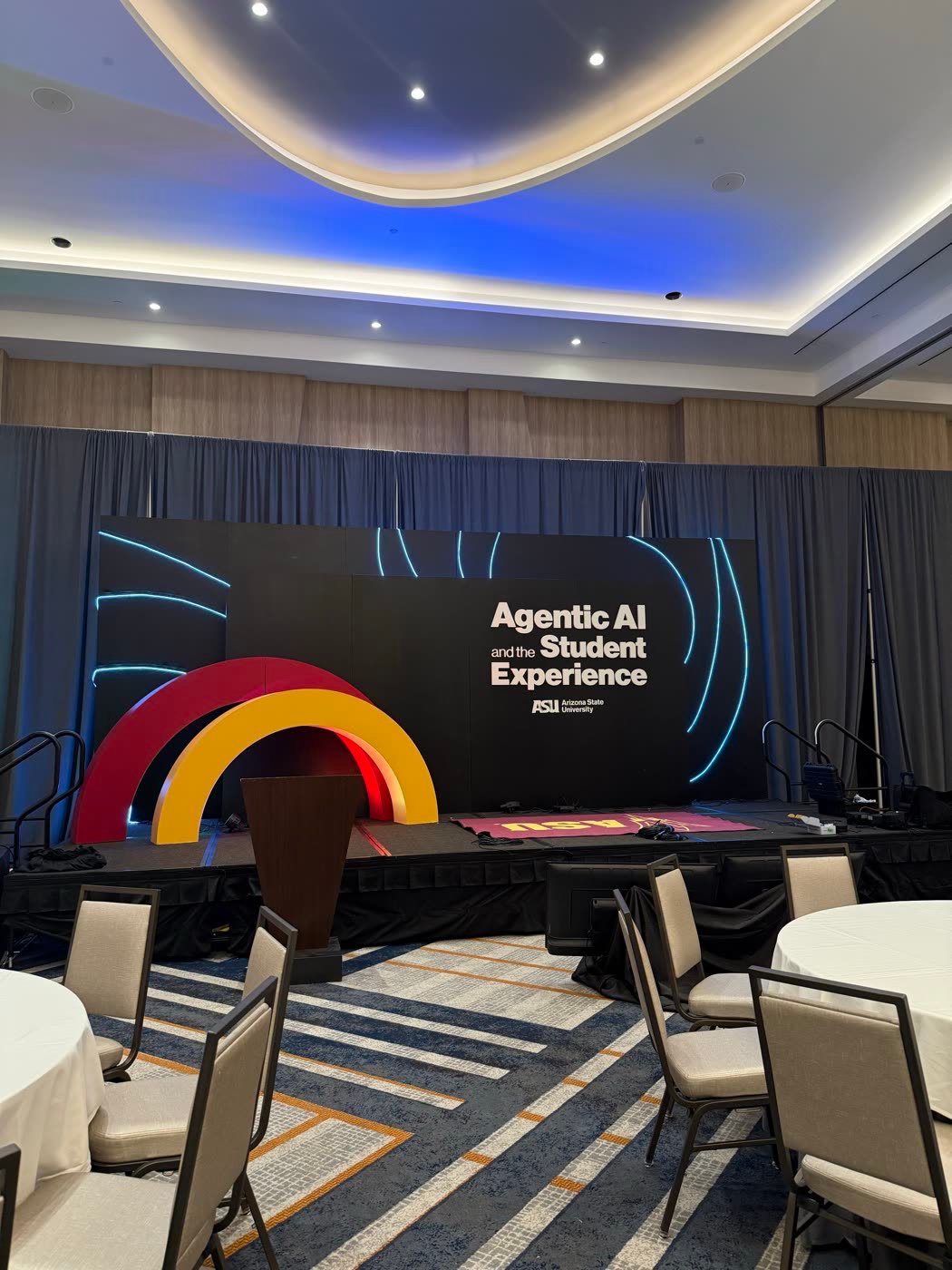 The main stage before doors open: black backdrop with neon arcs and the event title, gold and red arch set pieces, and a podium