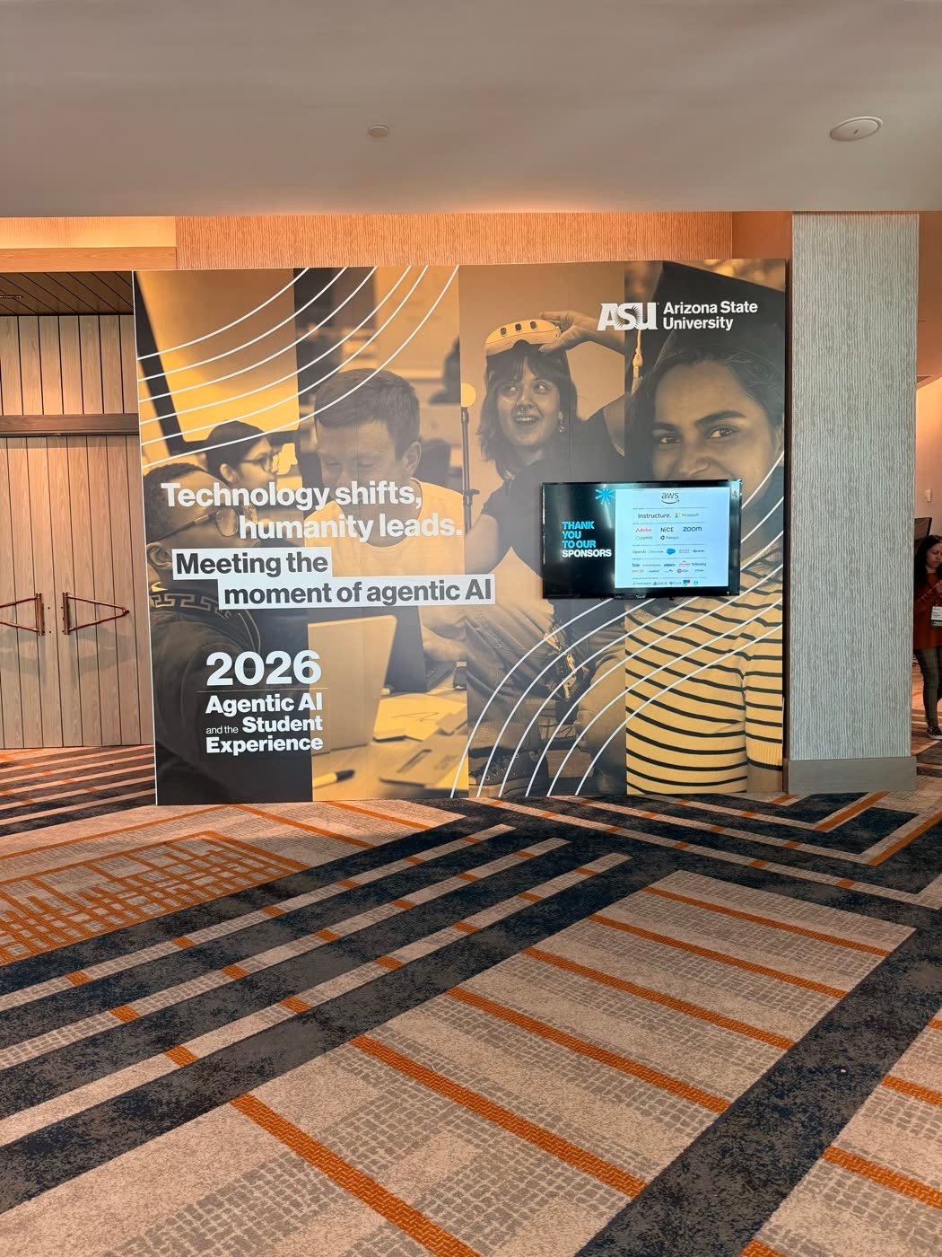 Entry wall reading Technology shifts, humanity leads. Meeting the moment of agentic AI, with student photos and a sponsor screen