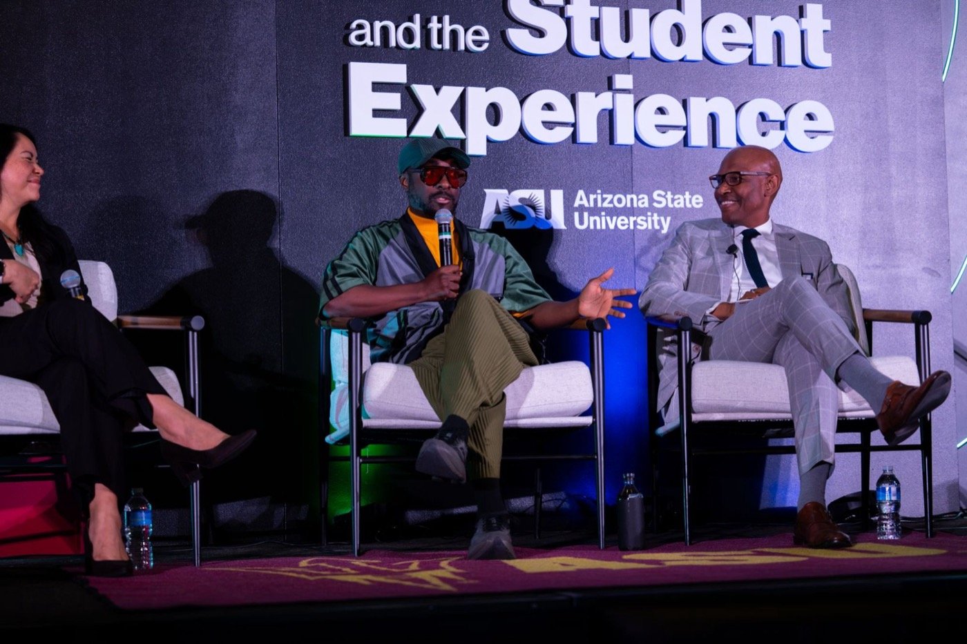 A three-person panel in lounge chairs on the main stage in front of the event title and ASU logo