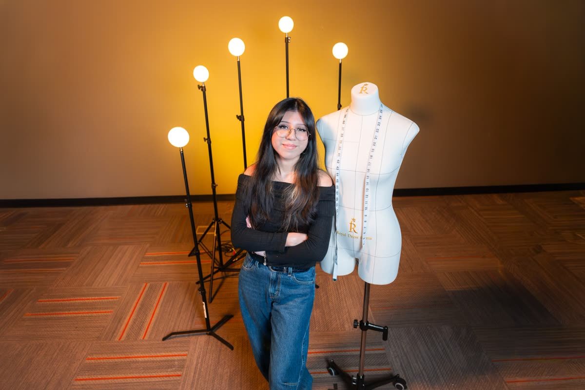 High-angle portrait of the cover subject with arms crossed next to a dress form and five globe lights