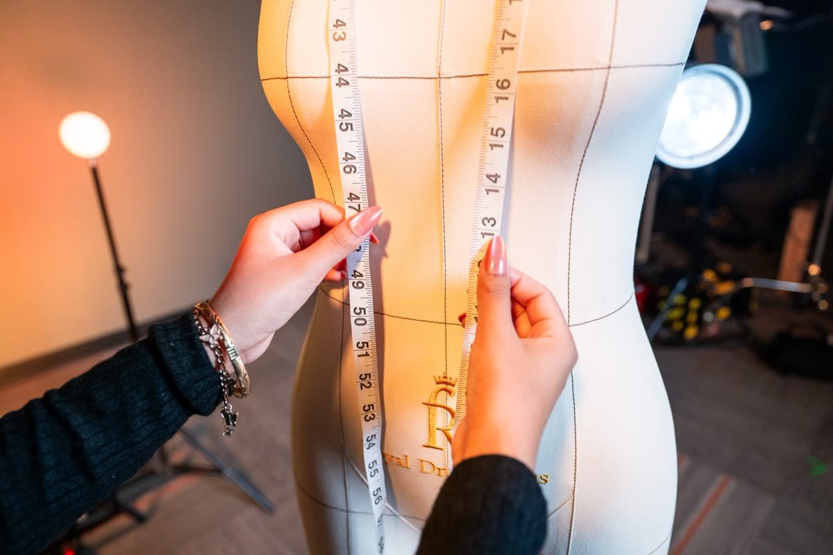Close-up of hands measuring a dress form with a tape measure