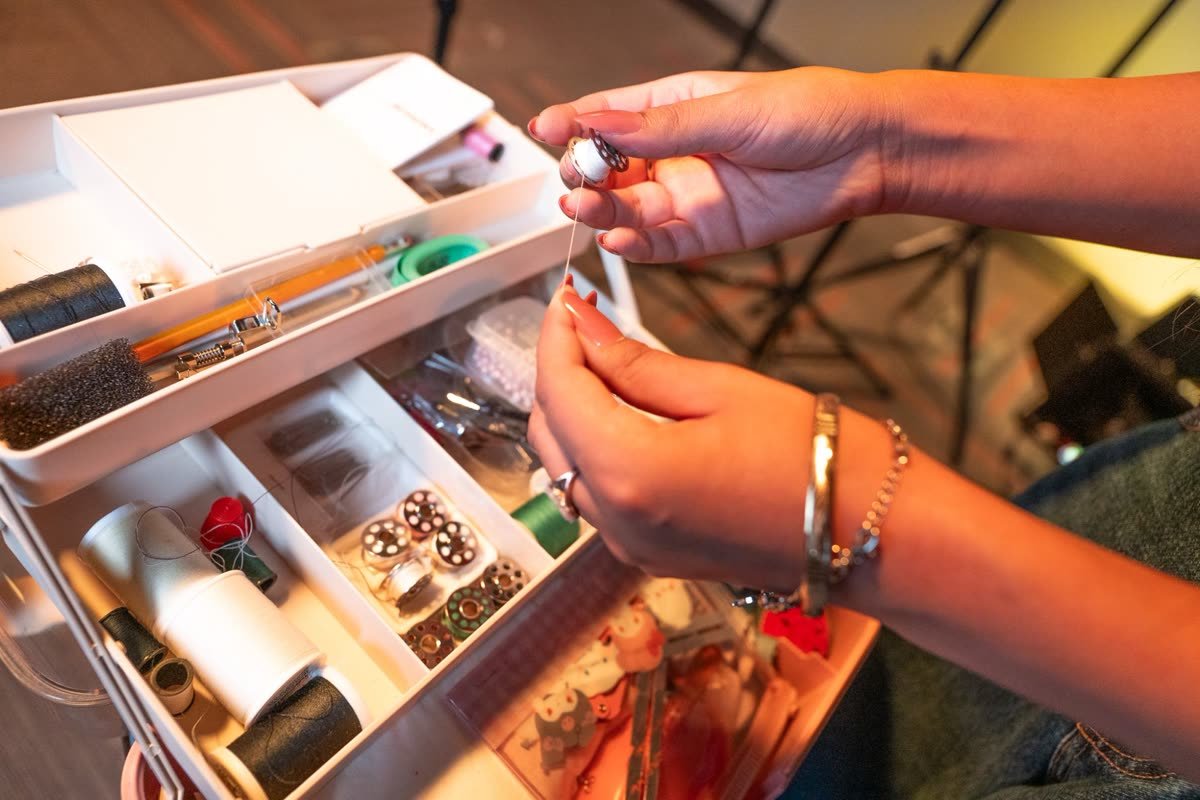 Close-up of hands threading a bobbin over an open sewing kit
